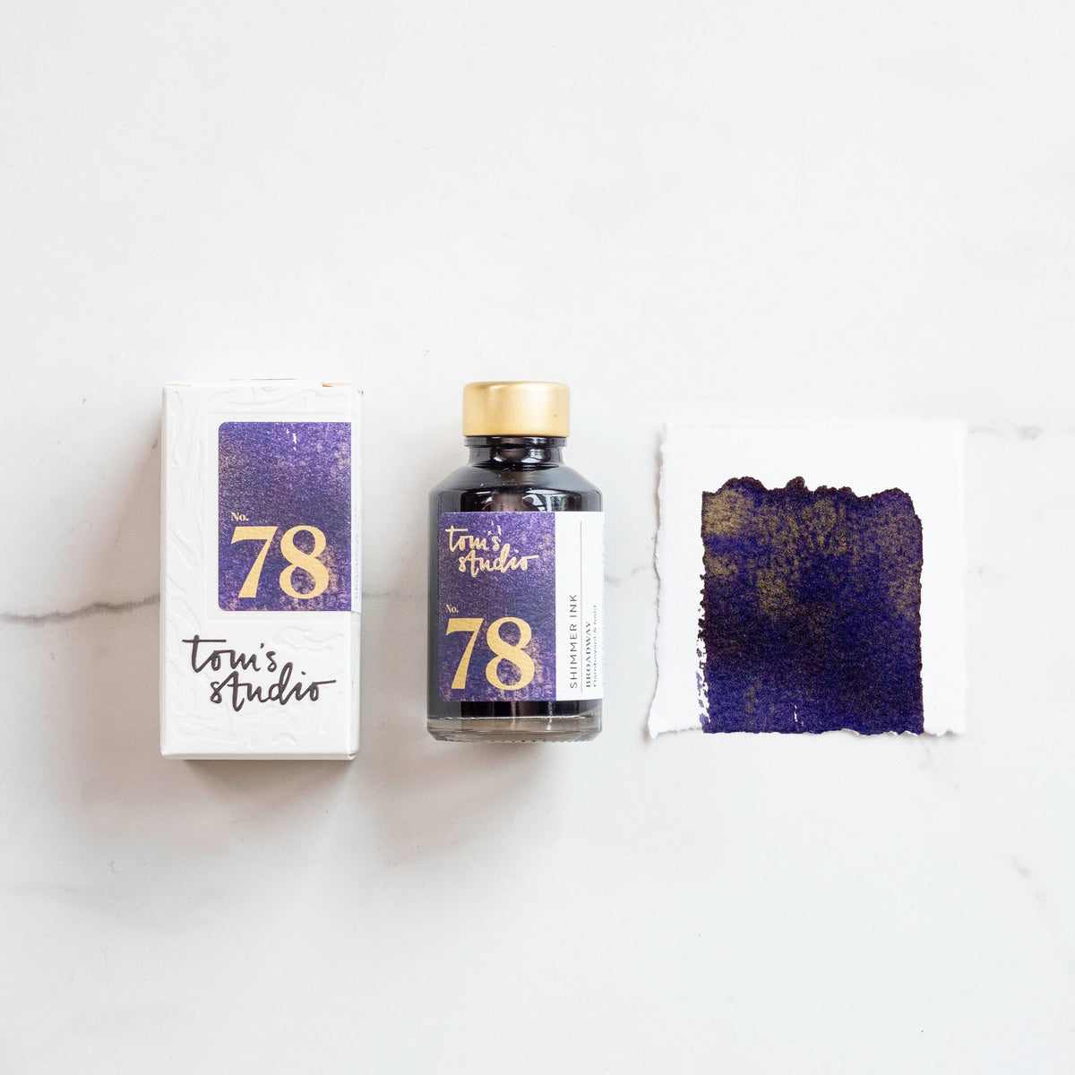 Tinta Tom’s Studio Shimmer 78 Broadway, com frasco, embalagem e amostra roxa com brilho dourado